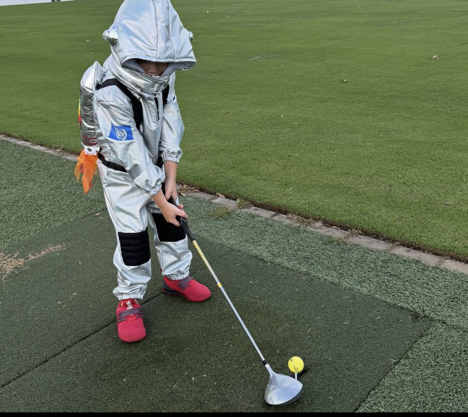 Kid in astronaut costume teeing off at Country Club of Louisiana driving range